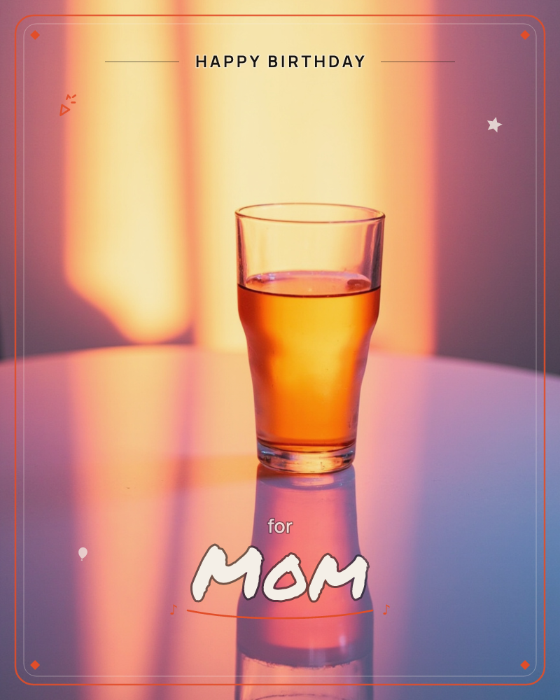 A single glass of amber liquid sits on a glossy tabletop, glowing against warm bands of orange and pink light streaming across the wall behind it, a birthday e-card design