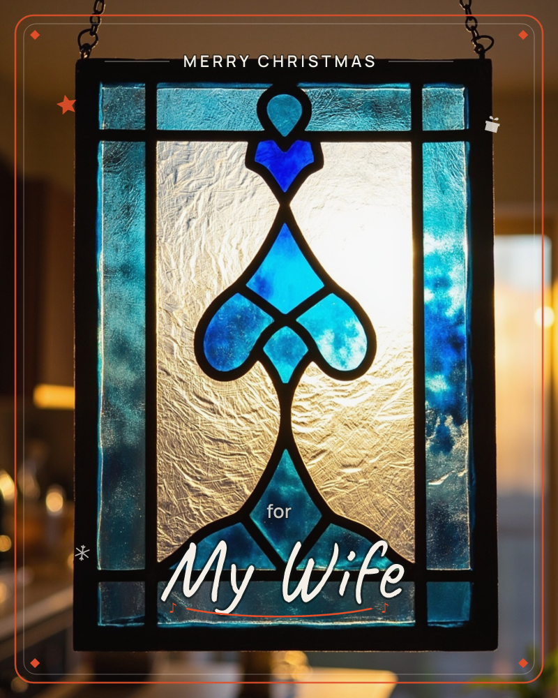 A stained-glass panel hangs on chains against a softly blurred indoor kitchen backdrop, warm lamplight glowing through its textured clear glass centre, a christmas e-card design