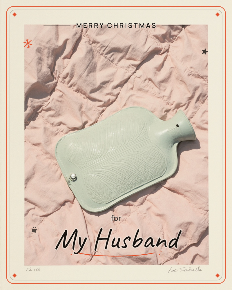 A sage-green rubber hot water bottle rests on a rumpled blush-pink quilted blanket, photographed from directly above in soft, even light, a christmas e-card design