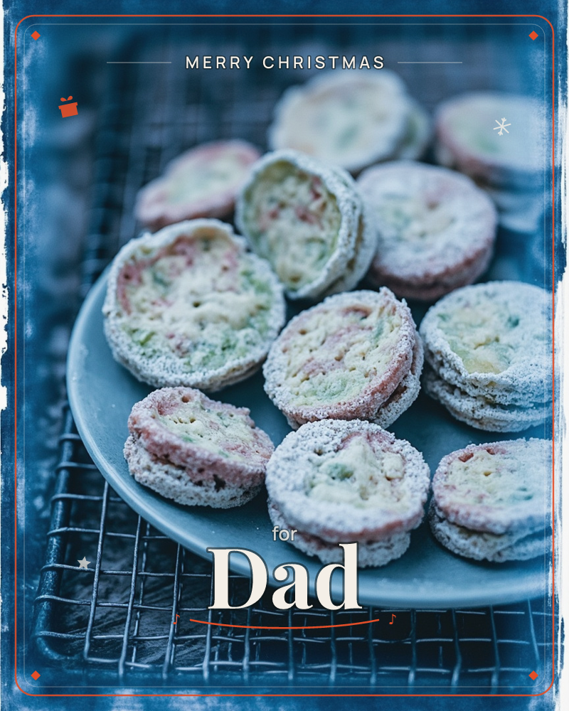 A blue-toned photograph shows a stack of round, sugar-dusted biscuits speckled with pink and green, piled on a matte blue plate that sits on a wire…, a christmas e-card design