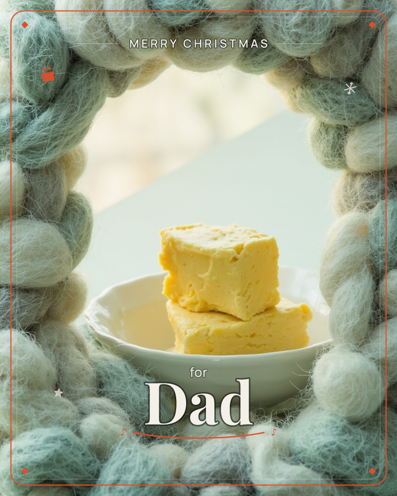 A chunky wreath of pale sage-and-cream wool loops frames a small white dish holding two golden squares of fudge or butter, lit softly against a pale…, a christmas e-card design