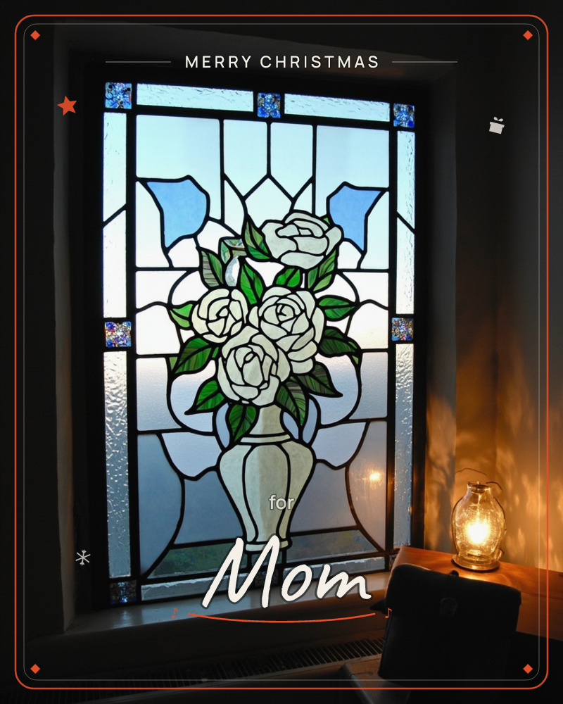 A stained-glass window depicts a vase of white roses with green leaves, framed in leaded panels of clear, textured and pale blue glass, a christmas e-card design