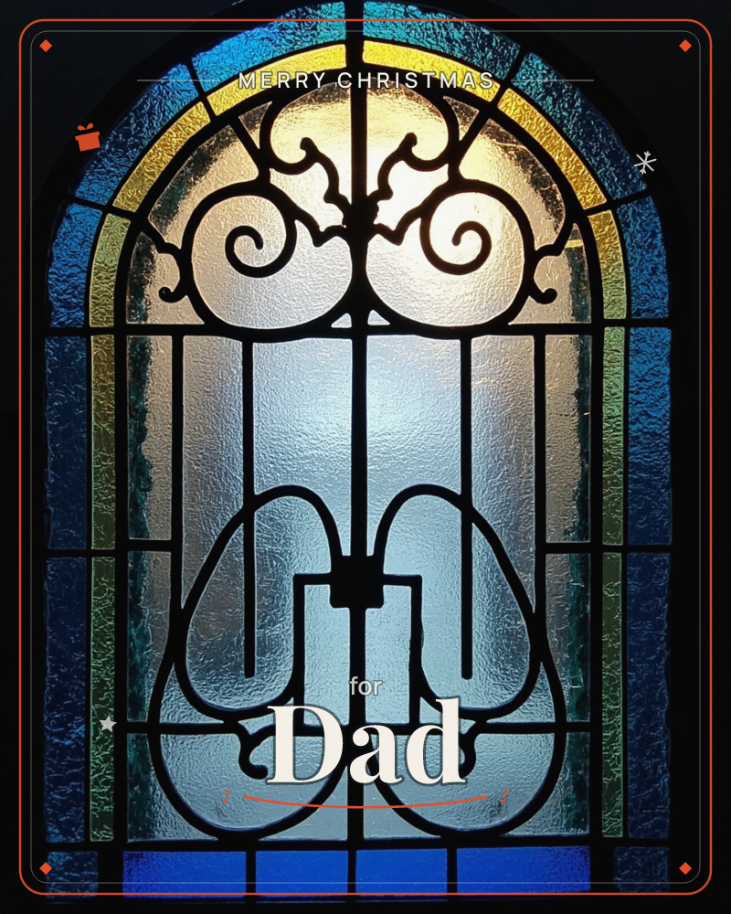 An arched stained-glass window glows from behind with warm golden light at its centre, framed by bands of deep blue, teal and yellow textured glass, a christmas e-card design
