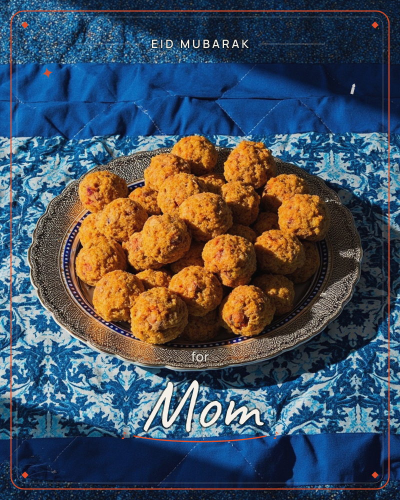 A silver-rimmed plate piled high with golden-orange sweet balls, textured and crumbly, sits on a richly patterned blue and white cloth, a eid e-card design