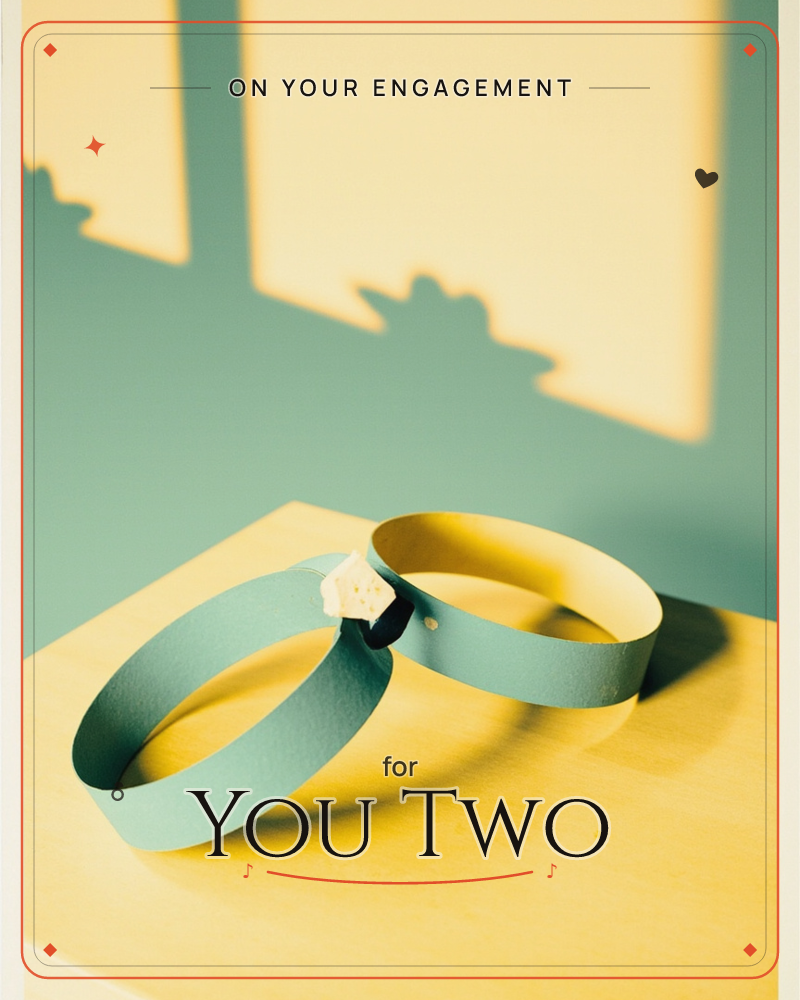 Two paper rings, one sage green and one buttery yellow, lean together on a warm gold surface with a tiny paper gem tucked between them, a engagement e-card design