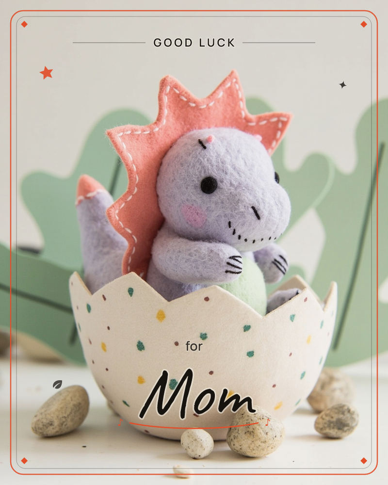 A felted purple dinosaur with a coral spiked back and rosy cheeks sits hatching from a speckled cream eggshell, cradling a small green egg in its paws, a good luck e-card design