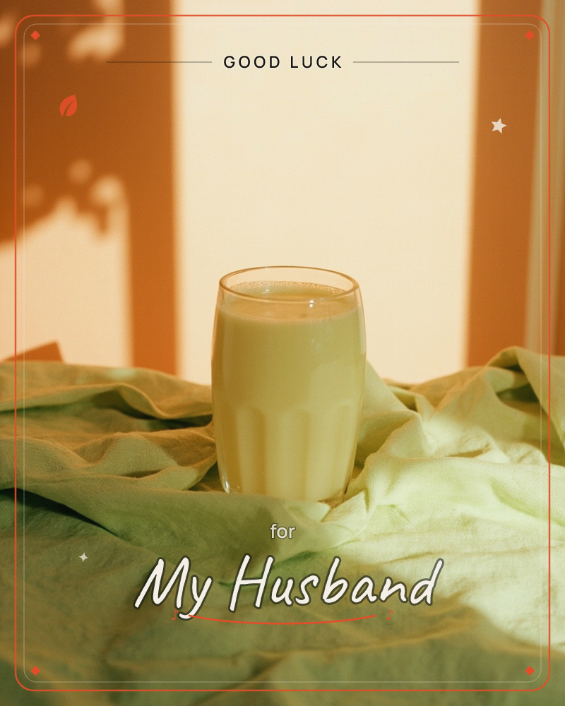 A ribbed glass of pale milky liquid sits on a rumpled sage-green cloth, warm sunlight throwing a leafy shadow across the terracotta wall behind it, a good luck e-card design