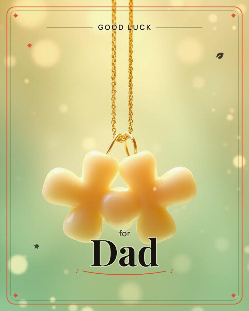 A gold chain necklace dangles two glossy cream-colored clover-shaped charms against a soft green and gold background scattered with glowing bokeh light, a good luck e-card design