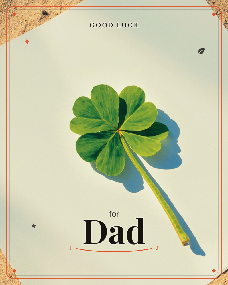 A single four-leaf clover with a long curved stem lies flat on a pale cream card, its long shadow stretching across the paper in bright, direct sunlight, a good luck e-card design