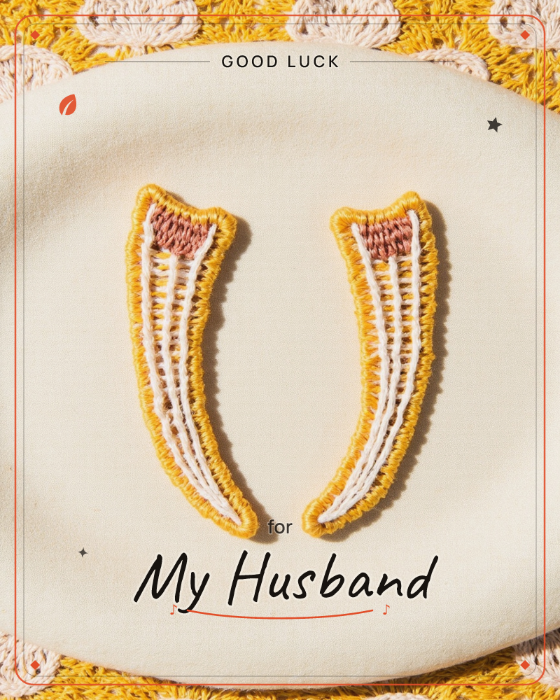 Two embroidered charms shaped like curved horns or tusks sit side by side on a cream oval patch, edged in golden-yellow thread with white ribbed…, a good luck e-card design