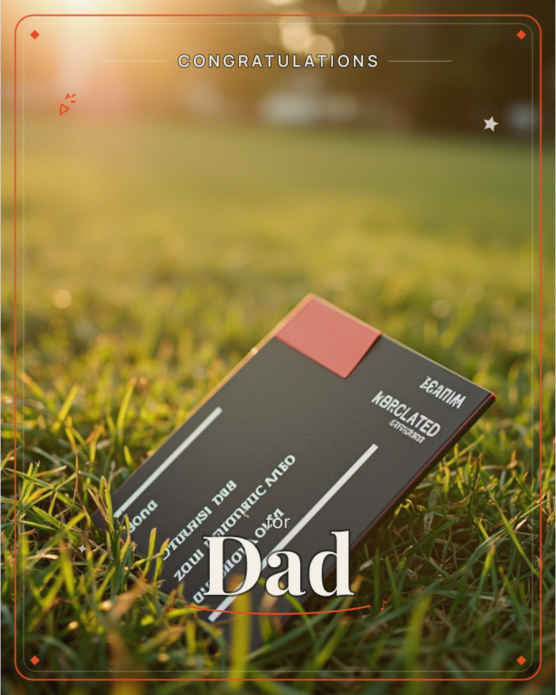 A dark card with a small red corner accent and pale printed lines of text rests propped in a lawn of green grass, caught in warm golden-hour light, a graduation e-card design