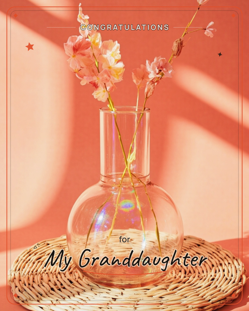 A round-bellied glass vase holds two slender cherry blossom sprigs, sitting on a woven rattan mat against a warm terracotta wall, a graduation e-card design