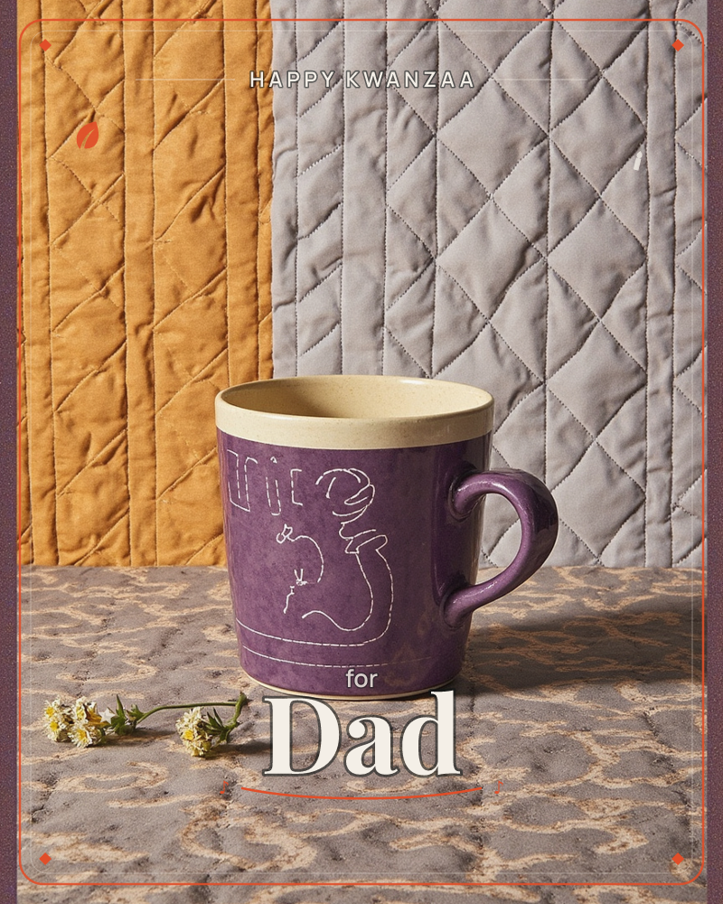 A deep purple ceramic mug with a cream rim and a hand-etched line drawing of a curled figure sits on a patterned stone surface, a kwanzaa e-card design
