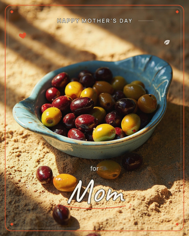 A weathered blue ceramic dish sits on sun-warmed sand, filled with a mix of glossy olives in deep burgundy, gold, and green tones, a mothersday e-card design