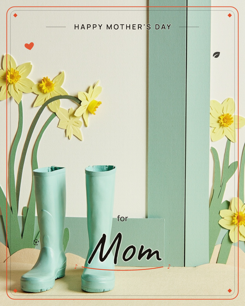 A pair of mint-green rubber boots stands on a sandy paper stage, surrounded by cut-paper daffodils in pale and bright yellow with stitched-looking centres, a mothersday e-card design