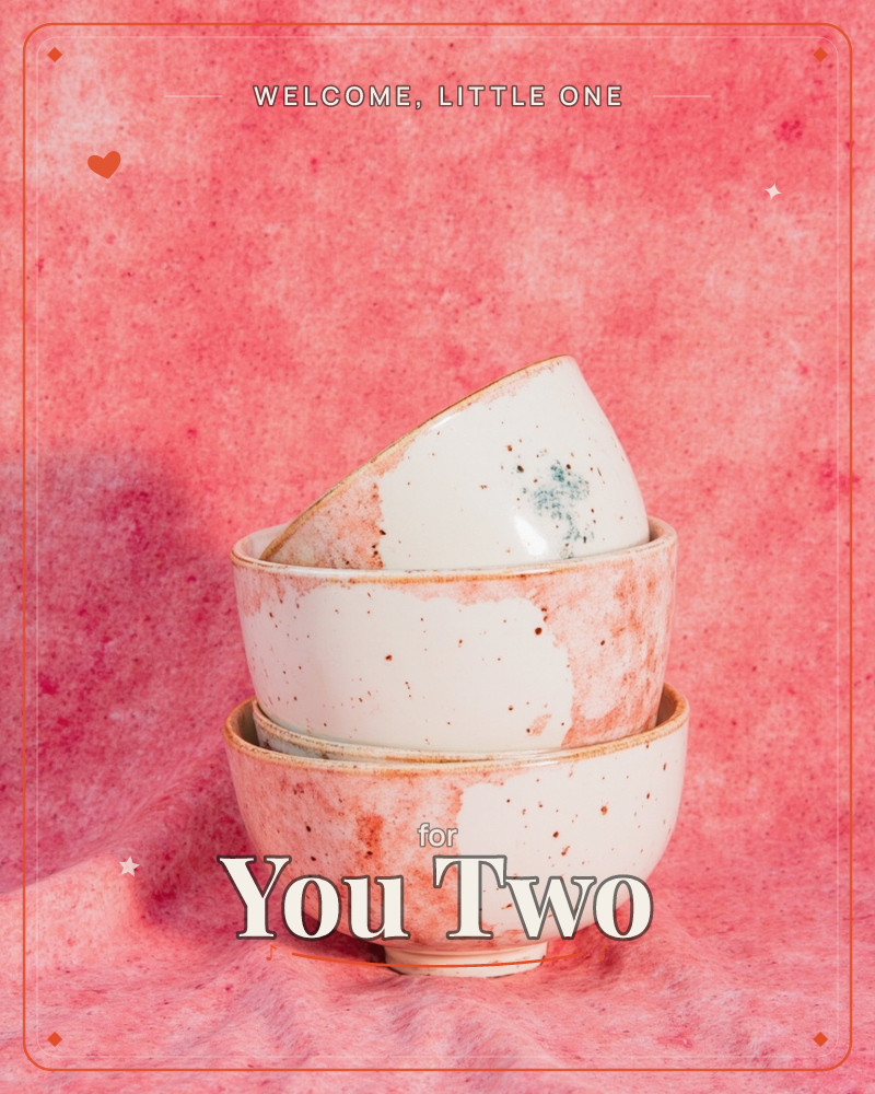 A stack of three handmade ceramic bowls, each glazed in speckled cream and rust-pink, tilts slightly against a mottled pink textile backdrop, a new baby e-card design