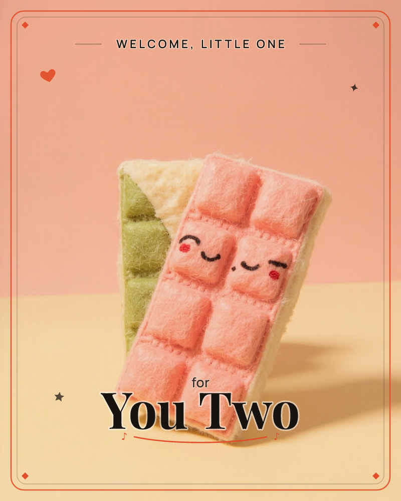 Two felt chocolate bars, one in soft pink and one in matcha green, lean together against a peach-and-cream backdrop, a new baby e-card design