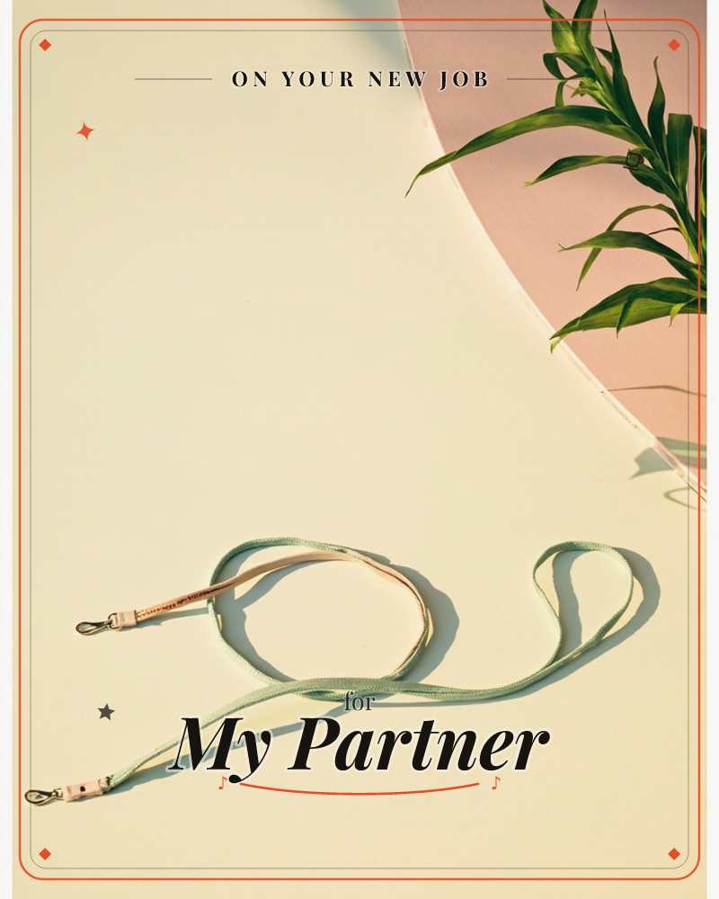 A cream tabletop catches hard afternoon light, with a sage-green and pale pink strap looped loosely across it, its metal clasps glinting, a new job e-card design