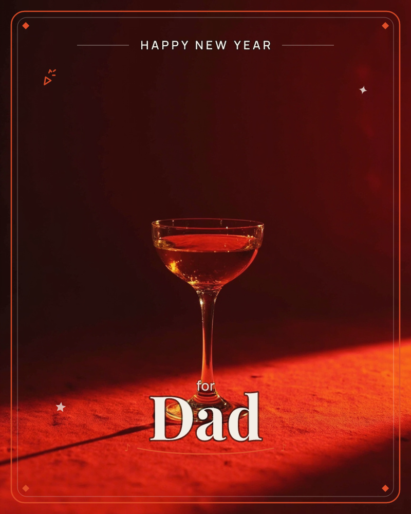 A coupe glass sits half full of pale gold liquid on a rough textured surface, caught in a diagonal shaft of deep red light against near-black shadow, a new year e-card design