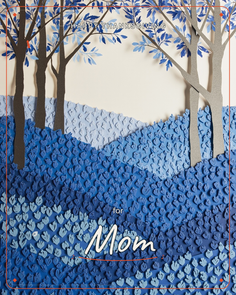 A layered paper-craft landscape rendered entirely in shades of blue, with cut-paper tree trunks rising into leafy canopies against a cream sky, a thanksgiving e-card design