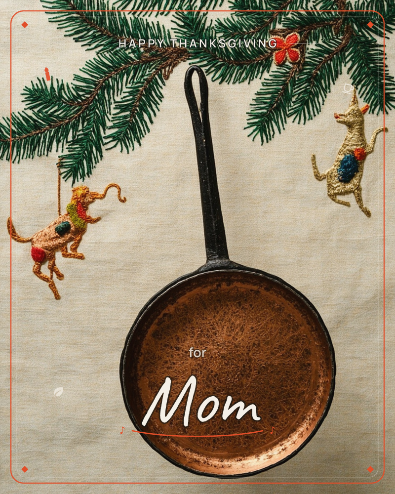 A small cast-iron skillet sits on a linen cloth embroidered with pine branches, a tiny red flower, and two whimsical trotting dogs in gold and blue thread, a thanksgiving e-card design